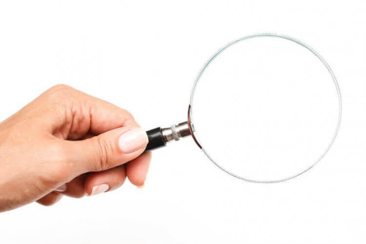 Closeup to a young woman's left hand holding a magnifying glass against a white plain background.
