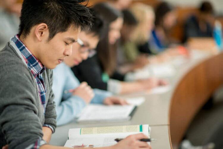 A row of college students sitting in class reading textbooks to illustrate 5 Insurance Options for College Students