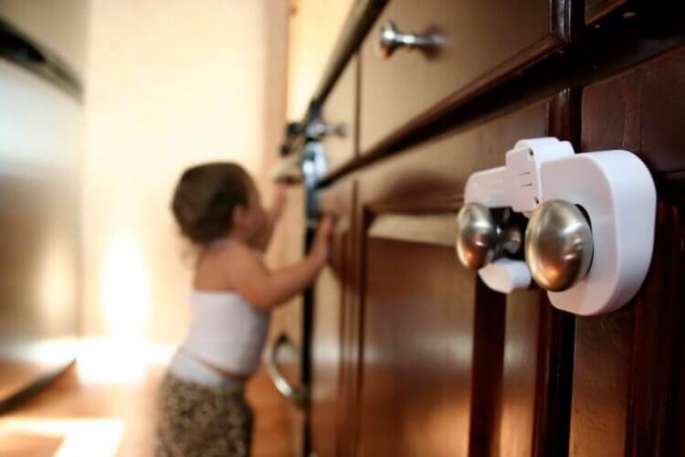 A toddler trying to open a kitchen cabinet illustrates Tips and Tricks to Help You Baby-Proof Your Home, One Room at a Time