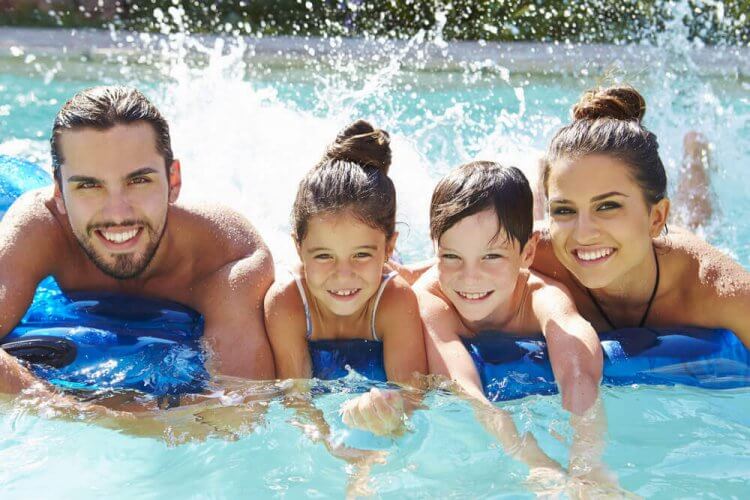 Portrait Of Family on Inflatable Raft in Swimming Pool illustrating tips for summer proper sun protection.