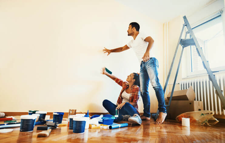 Young couple about to paint walls of new apartment. Many paint cans on the floor. A ladder behind them