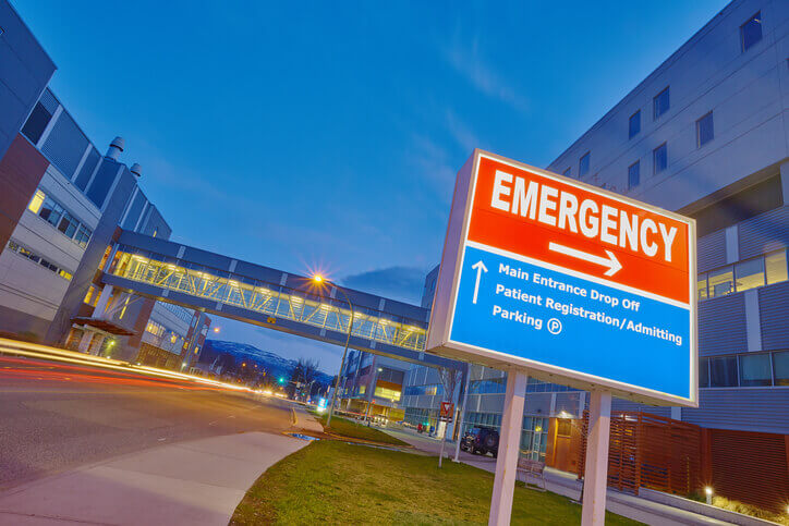 Emergency road sign before a hospital. In background, evening sky and closed, illuminated bridge communicating 2 hospital wings.