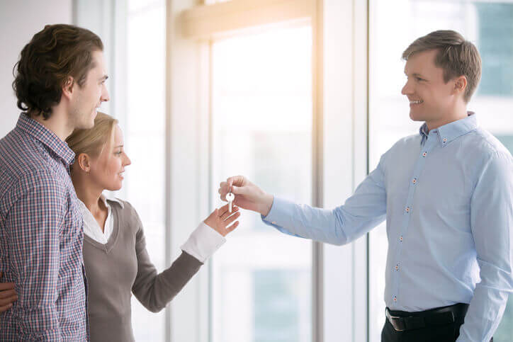 Happy young couple receiving key for new apartment from smiling young male real estate agent.