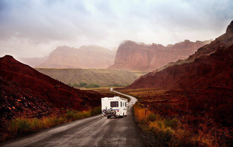 Motor home driving away on the road touring Utah, USA. A canyon and clouds in the background.