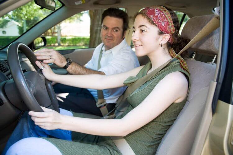 Teen girl taking driving lessons from her father and showcasing teenage driver insurance