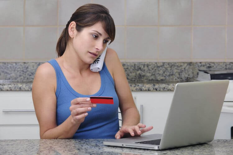 Concerned woman at home looking at laptop and holding credit card to illustrate steps to take if you've been the victim of identity theft.