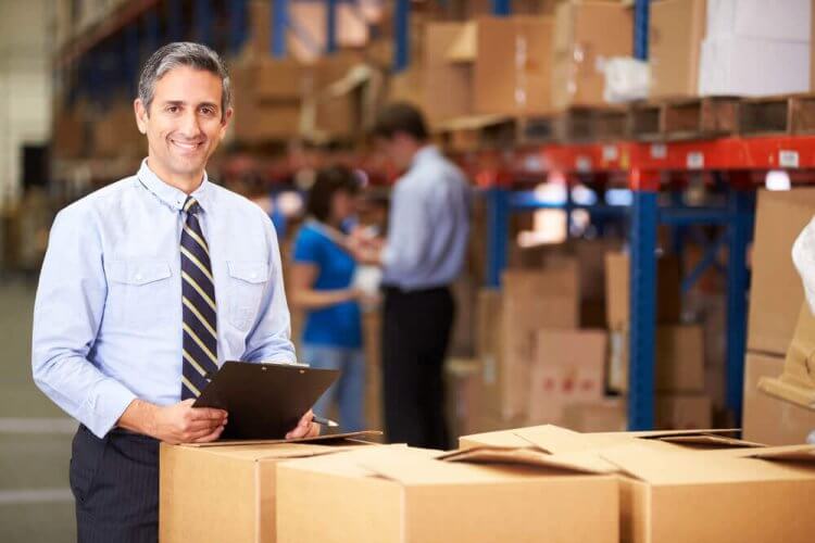 Business owner in warehouse holding clipboard surrounded by boxes to showcase why commercial insurance is important