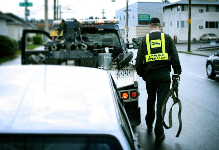 Rear view of a male roadside assistance professional who just hooked up a broken down car to his tow truck.