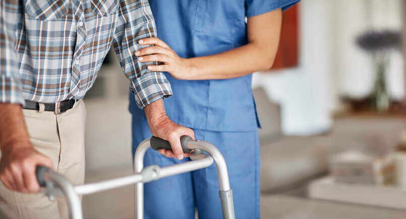 Young female nurse assisting her elderly male patient who's using a walker for support
