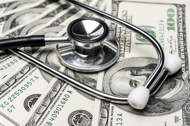 Close up to stethoscope on top of a pile of 100 dollar bills to illustrate expensive hospital stays