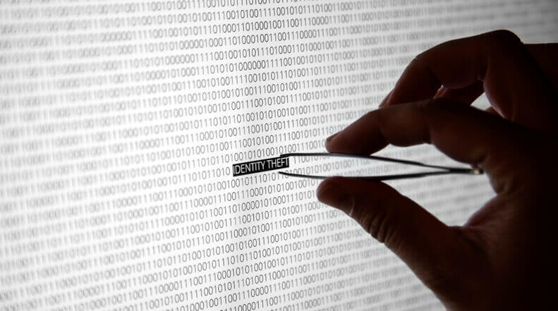 Close up to a hand in shadow holding tweezers holding the words identity theft.