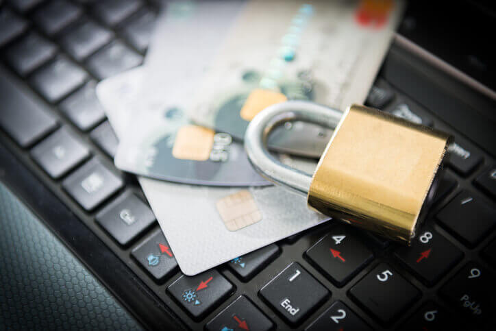 Security lock and stack of 3 credit cards on top of laptop keyboard to illustrate identity theft insurance.