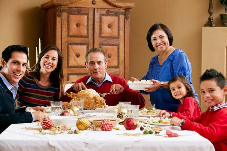 3 Generation family celebrating with Christmas meal smiling to camera. Christmas spheres decorate table.