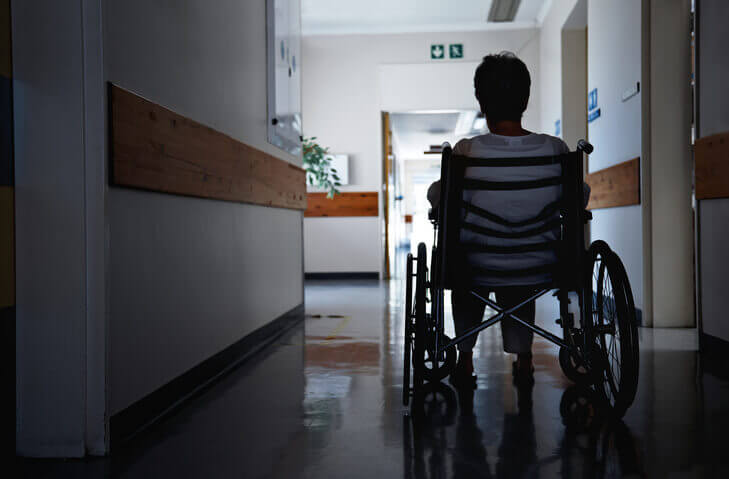 Rear view shot of a senior woman sitting in a wheelchair in the hall of a hospital.