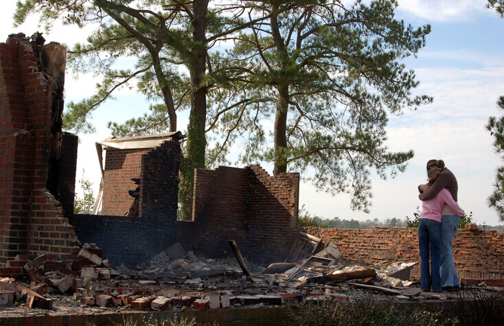 Picture of young couple hugging each other as they see their destroyed home after a natural disaster.