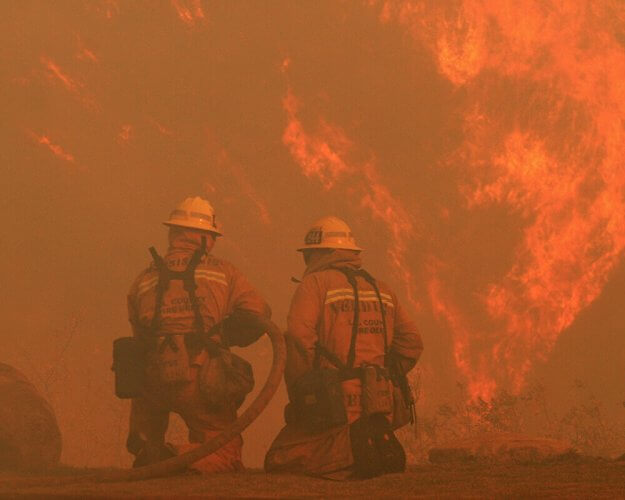 Rear view shot of two firemen fighting big flames in front of them during the Klamathin Fire in California.