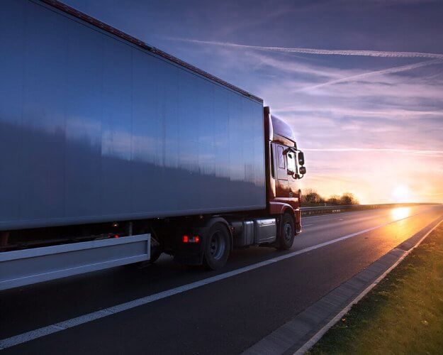 Side portrait of a large truck on empty highway during sunset.