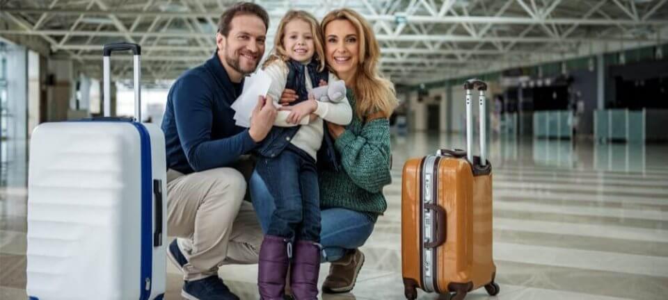 Young parents hugging their daughter at the airport, excited because they are going on a holiday trip. Two pieces of luggage beside them.