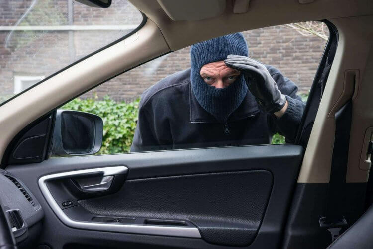 Burglar with a covered face and gloves peeks through passenger's window of a parked car.