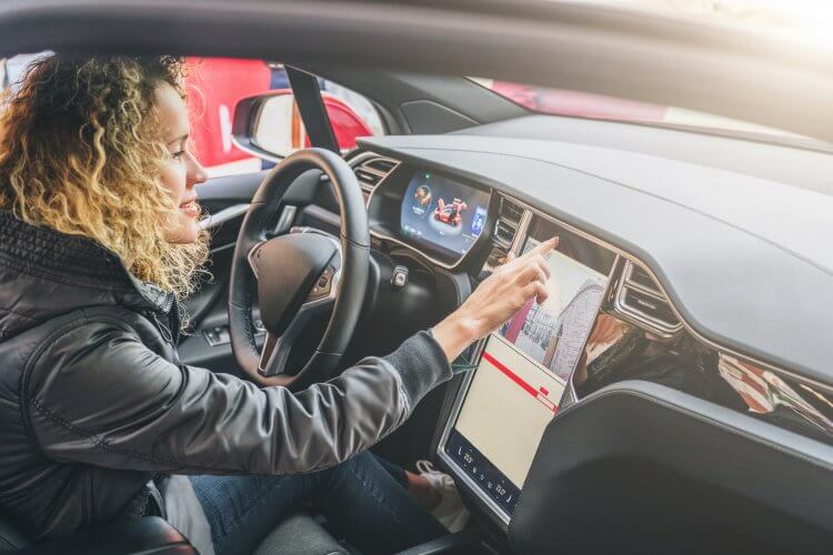 Young female driver smiling, programming something on her car's touchscreen.