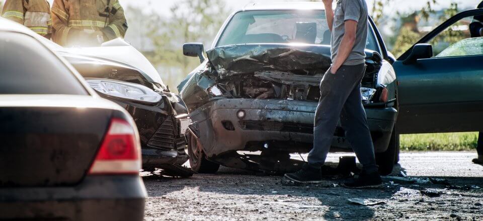 Shot of a car accident including a man on the phone walking towards two firefighters.
