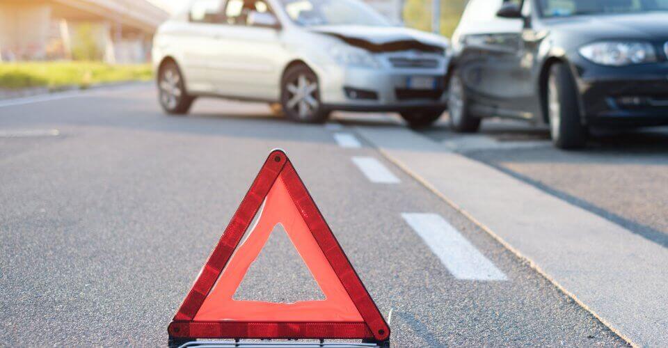 An emergency triangle on the road with a car crash in the background to illustrate what happens if you get caught driving without insurance in Oklahoma.