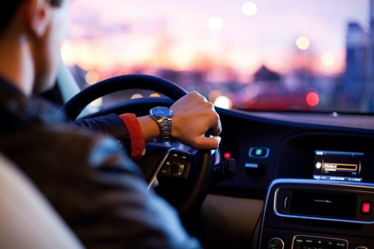 A man driving in a sunny afternoon with his left hand on the steering-wheel.