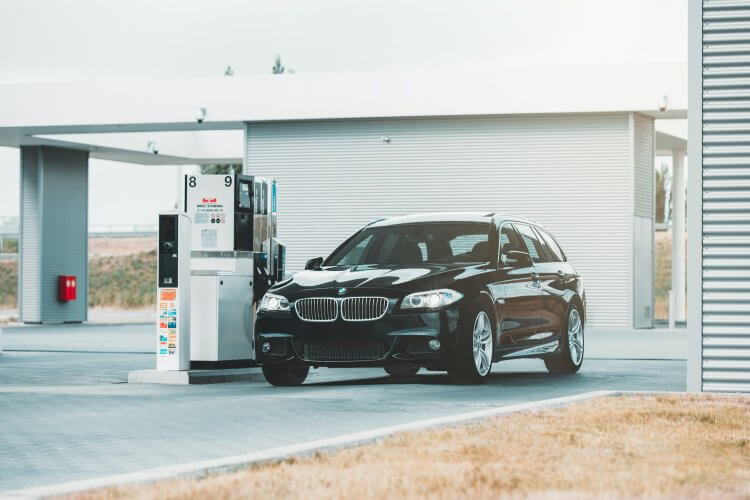 A black BMW 5 Series at the gas station waiting to be fueled.