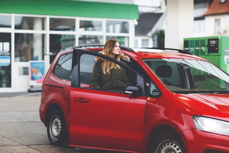 Young woman gets out of her car by gas station to refill car with gas.