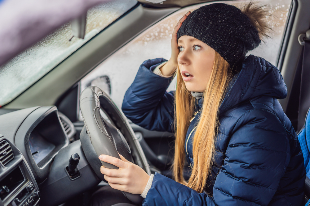 Woman in a car during a snowfall, thinking about roadside assistance safety tips