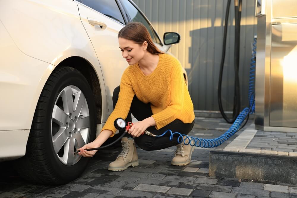 Young woman puts air in her car while keeping an eye on the air pressure gauge - cheap car insurance.