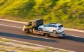 Grúa transportando un auto blanco por carretera, una solución práctica para transportar auto de un estado a otro en Estados Unidos.
