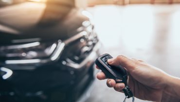 Persona sosteniendo el control remoto de un automóvil frente al vehículo estacionado, listo para conducir después de completar el registro y seguro del carro en Estados Unidos.