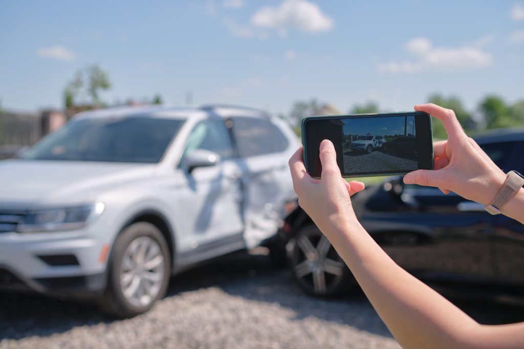 Persona tomando fotos de un accidente de auto para documentar daños, ejemplo de un evento imprevisto que suele estar cubierto por un seguro, no por una garantía.