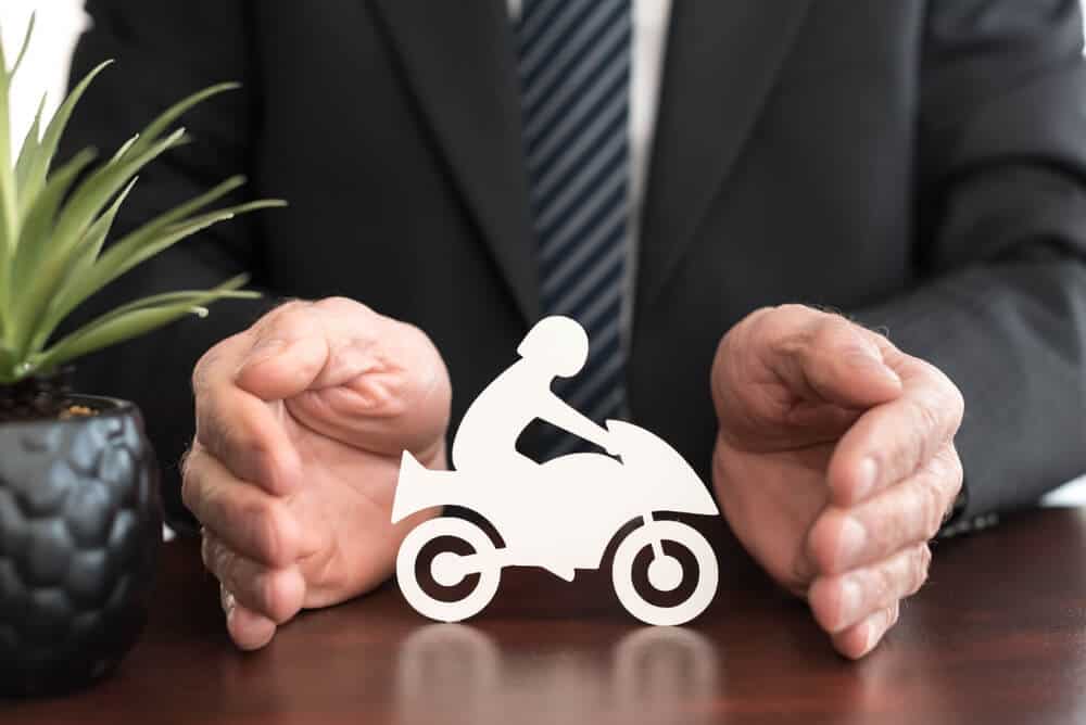Un hombre con traje protege con sus manos un ícono de motocicleta, representando los distintos tipos de cobertura para motocicleta en seguros
