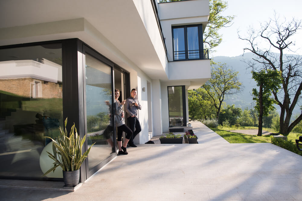 Una pareja está de pie frente a su casa moderna, representando la diferencia entre cobertura amplia vs limitada en seguros para proteger el hogar.