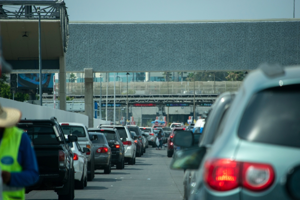 Fila de autos en cruce fronterizo entre Estados Unidos y México, mostrando el proceso de viajar con residencia americana por tierra.