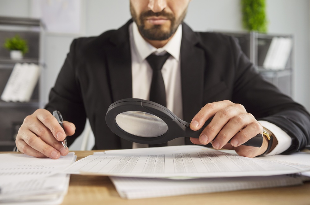 Un agente revisa cuidadosamente documentos con una lupa durante el proceso de verificación, ilustrando cómo las aseguradoras pueden detectar información falsa o inconsistencias en una póliza.