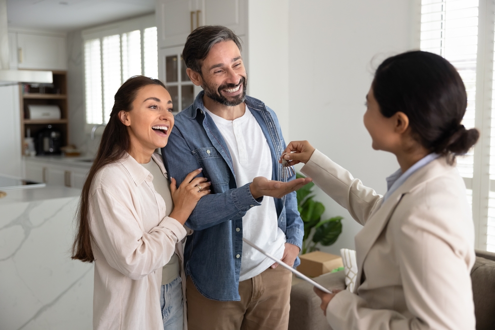 Una pareja recibe las llaves de su nuevo hogar de manos de una agente inmobiliaria, un momento que refleja la importancia de revisar el contrato y conocer las condiciones del alquiler antes de rentar una casa en Estados Unidos.