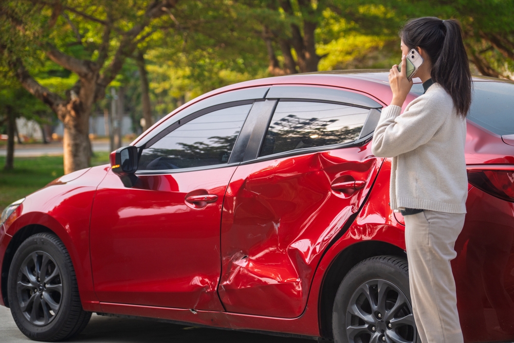 Conductora llama por teléfono tras un accidente con daños visibles en su vehículo, ejemplo de una situación en la que un seguro de auto puede ofrecer respaldo financiero y asistencia inmediata.