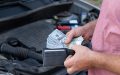 Persona sostiene dinero frente al motor de un automóvil, ilustrando el reto de cubrir reparaciones con ahorros propios en lugar de contar con un seguro de auto.