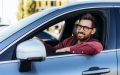 Hombre sonriente al volante de su auto, relacionado con pagar el seguro de auto por adelantado.