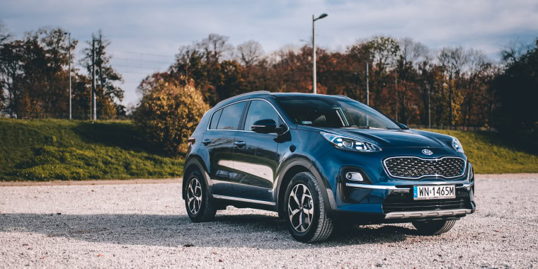 Kia Sportage azul parqueado frente a árboles.