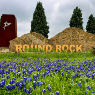 Señal monumental en la entrada a la ciudad rodeada de campo de flores azules. Round Rock, Texas – Freeway, seguro de auto barato en Round Rock, Texas.