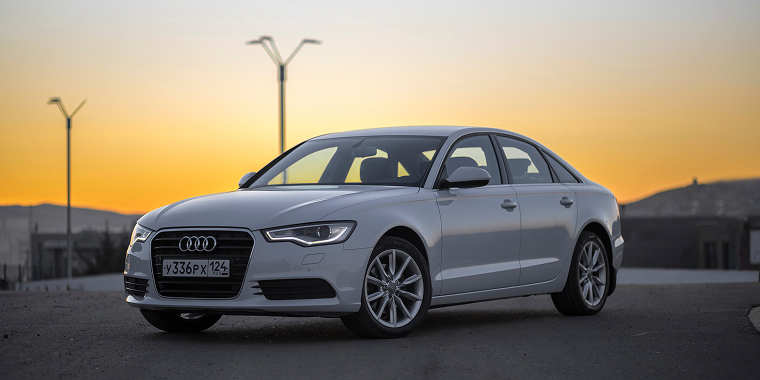 Audi A6 color blanco estacionado en un atardecer.