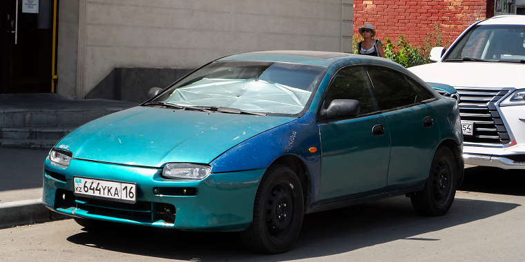 Mazda Protege verde estacionado en una calle residencial – seguro de auto barato para Mazda