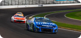 Dos autos de carrera NASCAR circulan a alta velocidad en una pista, incluyendo un auto azul con la marca Freeway Insurance liderando.