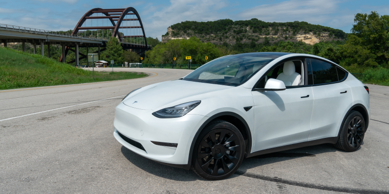 Tesla Model Y blanco estacionado cerca de un puente en una carretera abierta, representando viajes en vehículo eléctrico moderno.