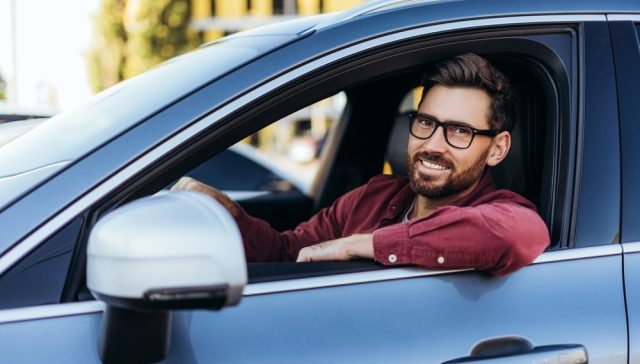 Hombre sonriente al volante de su auto, relacionado con pagar el seguro de auto por adelantado.