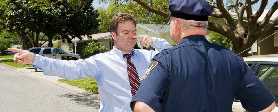 A middle-aged Caucasian driver stands in front of a police officer trying to prove that he did not commit a DUI.